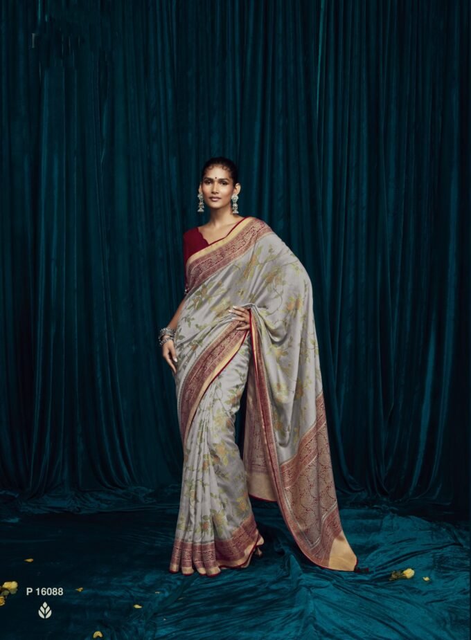 Elegance meets sophistication in our graceful Grey Soft Brasso Silk saree, a symbol of refined style and timeless beauty. This exquisite saree is expertly crafted, featuring a striking red designer blouse and a custom-tailored finish adorned with an intricately detailed piped border. The subtle grey hue exudes understated charm, making it an impeccable choice for special occasions and celebrations. Every element of this ensemble reflects the artistry of traditional craftsmanship seamlessly merged with contemporary fashion. The handcrafted excellence of the saree ensures that you'll be the center of attention wherever you go, leaving a lasting impression. Elevate your style with this timeless piece that emanates beauty and poise, ensuring you stand out with unparalleled grace.